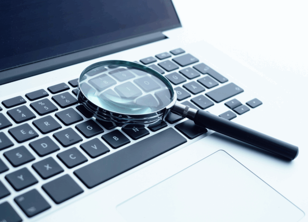 Lupa sobre teclado portátil simbolizando las herramientas digitales de trabajo de un detective privado